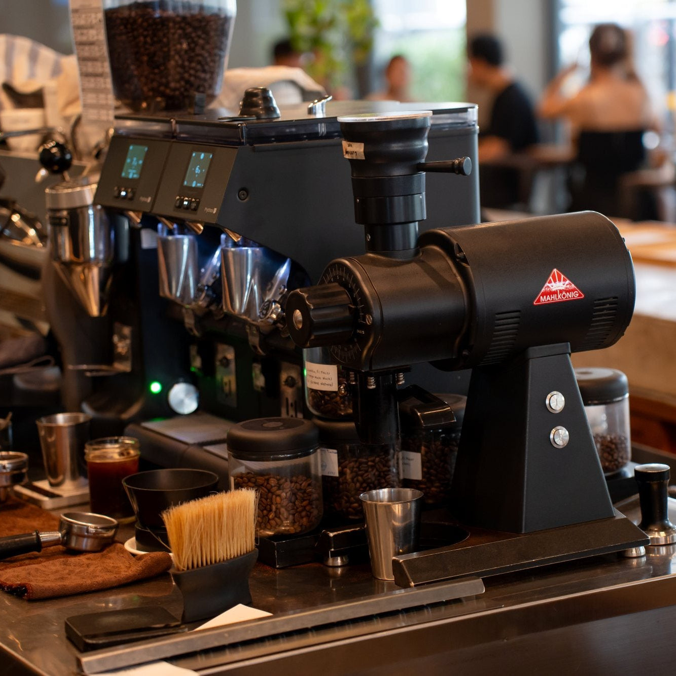 Commercial coffee grinder on a counter with blurred background of people and coffee shop setting