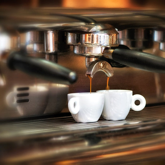 Espresso machine dispensing coffee into two white cups.