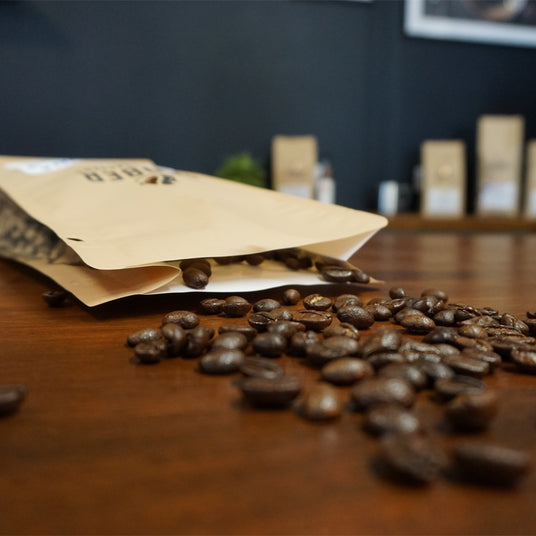 Coffee beans spilling out of a paper bag on a wooden surface with blurred background