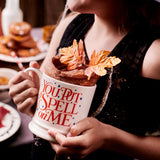 Person holding a mug with 'You Put a Spell on Me' text, blurred background
