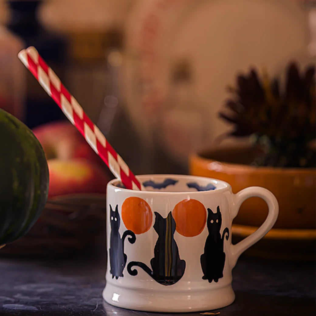 Ceramic mug with black cat and orange pumpkin design on a dark surface.