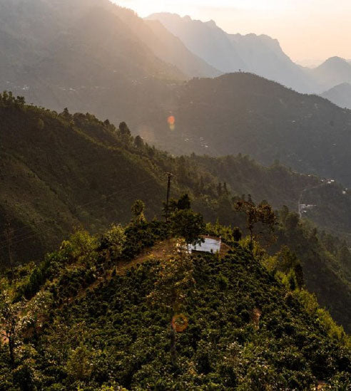 Scenic view of mountains with a house on a hill at sunset.