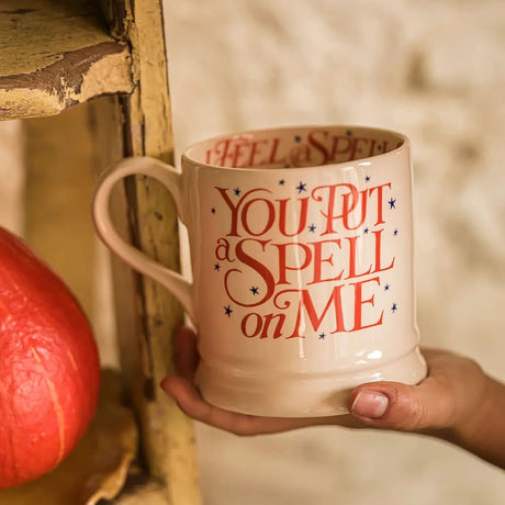Person holding a mug with 'You Put a Spell on Me' text next to a pumpkin.