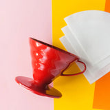Red coffee dripper and white filters on a colorful background