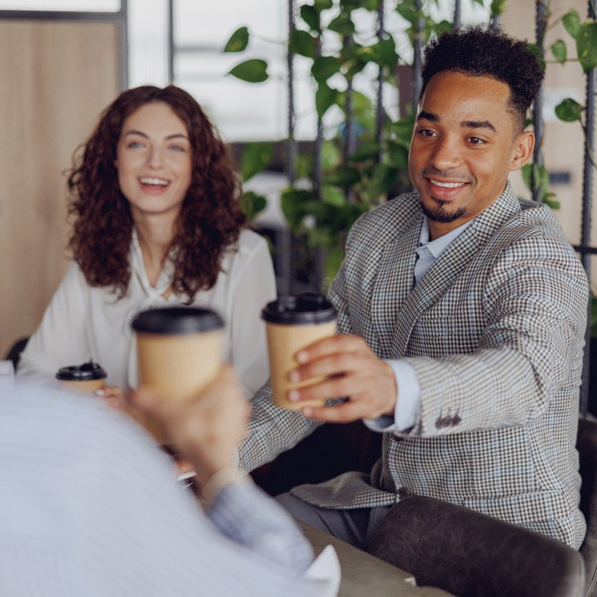 Two people sitting together, each holding a coffee cup, with a casual indoor setting.