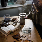 Person making coffee using a manual grinder and kettle on a wooden table.
