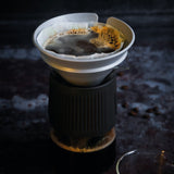 Coffee filter with coffee grounds and a cup of coffee on a dark surface