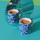Two blue floral-patterned mugs with coffee on a green and blue background