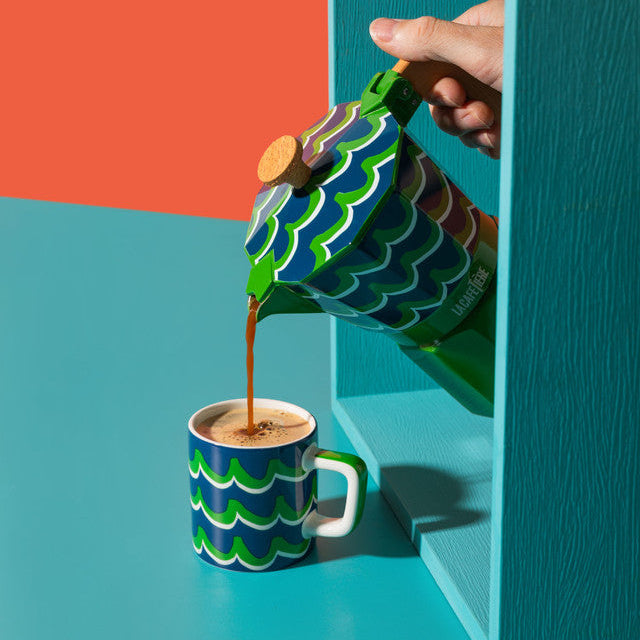 Colorful coffee pot pouring coffee into a matching cup against a vibrant background