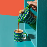 Colorful coffee pot pouring coffee into a matching cup against a vibrant background