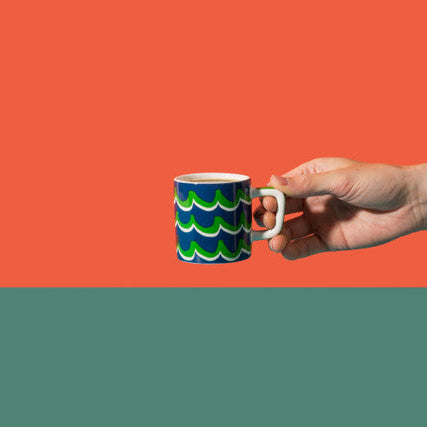 Hand holding a mug with wave design against an orange background