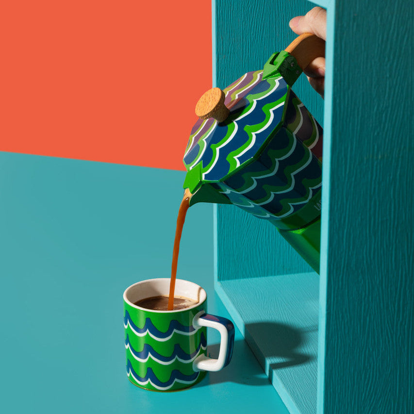 Colorful teapot pouring coffee into a matching cup against a vibrant background
