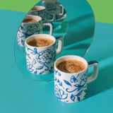 Two floral-patterned coffee cups on a teal surface with a green background