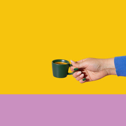Hand holding a green mug with a yellow and purple background
