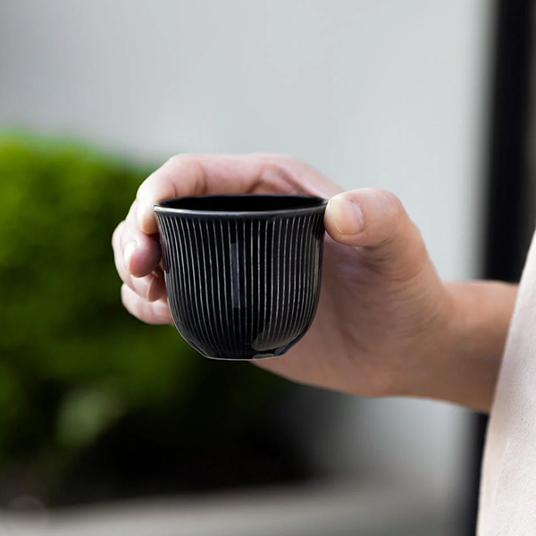 Hand holding a black ceramic cup with a blurred green background