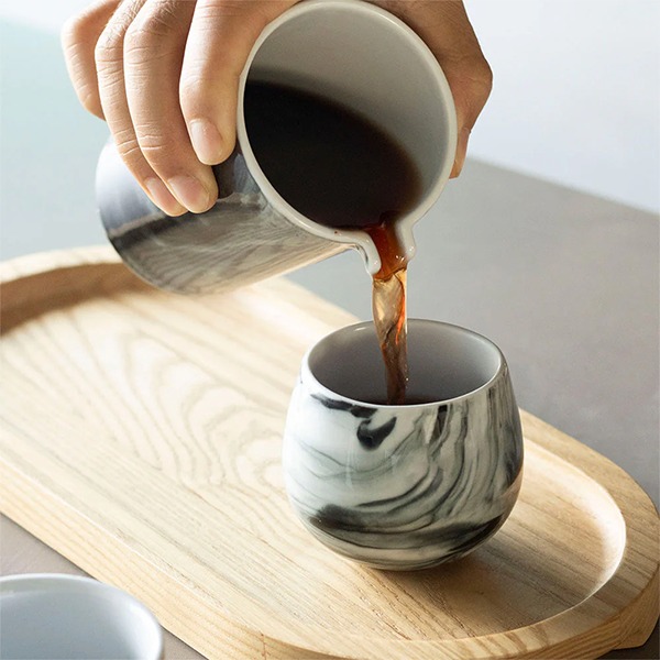 Marble-patterned cup being filled with dark liquid on a wooden tray.