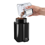 A hand pouring coffee beans from a transparent lid into the Melitta AMIGO Electric Blade Coffee Grinder, showcasing the grinder's compact black design and user-friendly bean container lid.