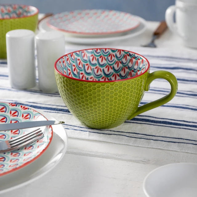 Green ceramic cup with colorful interior on a table setting with plates and cutlery.