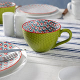 Green ceramic cup with colorful interior on a table setting with plates and cutlery.