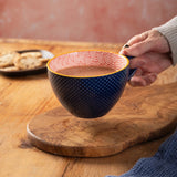 Person holding a blue mug with pink interior on a wooden surface