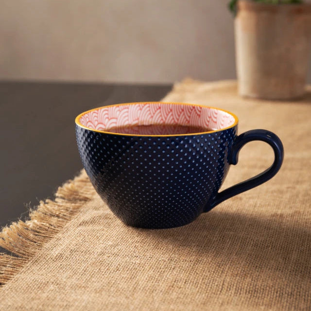 Navy blue textured mug with pink interior on a wooden surface, plant in the background
