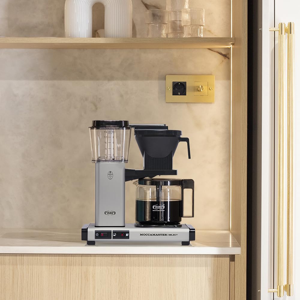 Moccamaster coffee maker on a kitchen shelf with a neutral wall and gold handle in the background.