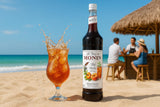 Monin syrup bottle with a glass of iced tea on a beach