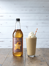 Bottle of Sweetlife syrup next to a glass of a milkshake with whipped cream on a wooden surface.