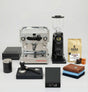 Coffee-making equipment including a espresso machine, grinder, and accessories on a white background