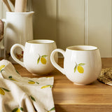 Sophie Allport Lemons stoneware mugs styled with a matching tea towel on a wooden worktop