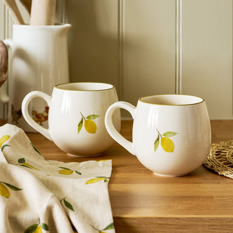 Sophie Allport Lemons stoneware mugs styled with a matching tea towel on a wooden worktop