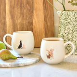 Sophie Allport Labradors & Retrievers mugs on a kitchen worktop beside pears, a wooden board and a green-speckled vase