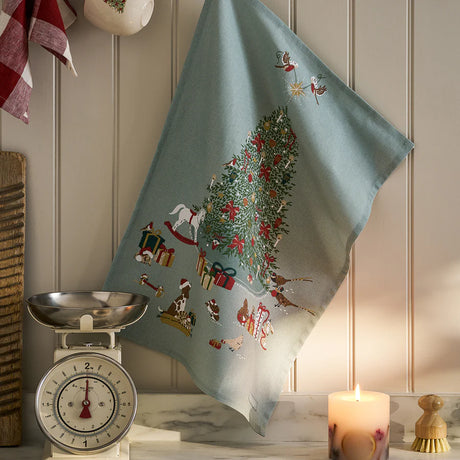 Decorative towel with Christmas tree design hanging on a wall next to a scale and candle.