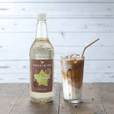 Bottle of Sweetピー syrup with a glass of iced coffee on a wooden surface.