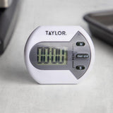 Taylor digital timer on a light gray surface with kitchen items in the background