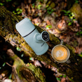 Turquoise coffee press and glass with coffee on a forest floor