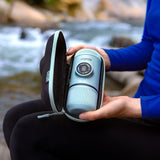 Person holding a portable shower device in front of a natural water background