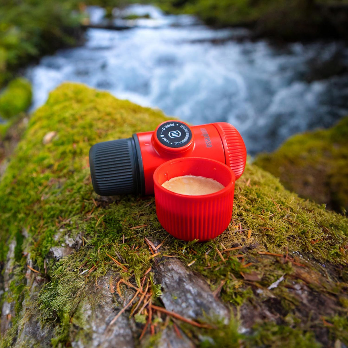 Red camping stove with a pot on a mossy rock with a stream in the background