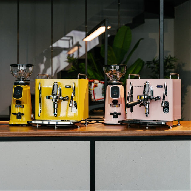 Two colourful coffee machines on a wooden table with a modern interior background.
