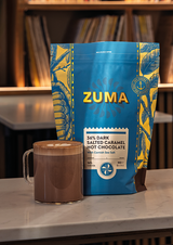 Zuma 60% Dark Salted Caramel Hot Chocolate package with a mug of hot chocolate on a table.