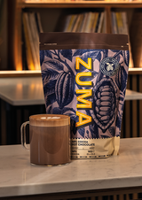 Zuma hot chocolate bag with a mug of hot chocolate on a surface.