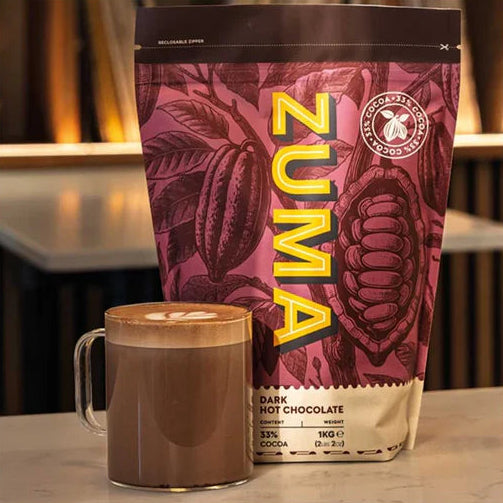 Zuma dark hot chocolate package with a mug of hot chocolate on a wooden surface.