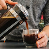 Person pouring coffee from a French press into a glass.