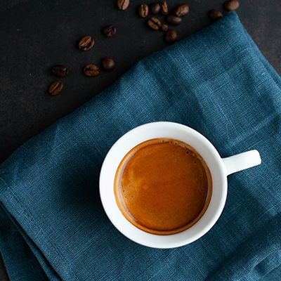 White cup of coffee on a blue cloth with scattered coffee beans