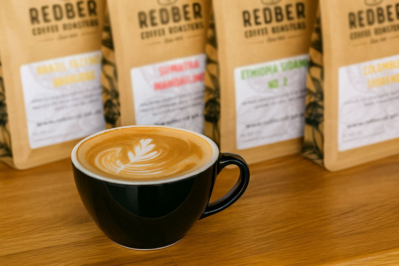 Black cup of coffee with latte art on a wooden surface, surrounded by Redber Coffee bags.