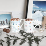 Sophie Allport Skiing design mugs filled with hot chocolate beside mountain photographs