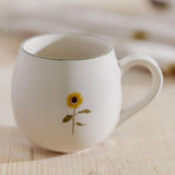 Close-up of Sophie Allport Sunflower stoneware mug on a wooden surface, showing the floral design and green rim
