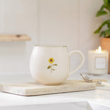 Sophie Allport Sunflower stoneware mug on a wooden board beside a spoon and lit candle