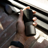 Hand holding a Wacaco Exagrind manual coffee grinder beside a window