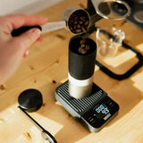 Adding coffee beans to a Wacaco Exagrind grinder at a coffee preparation station